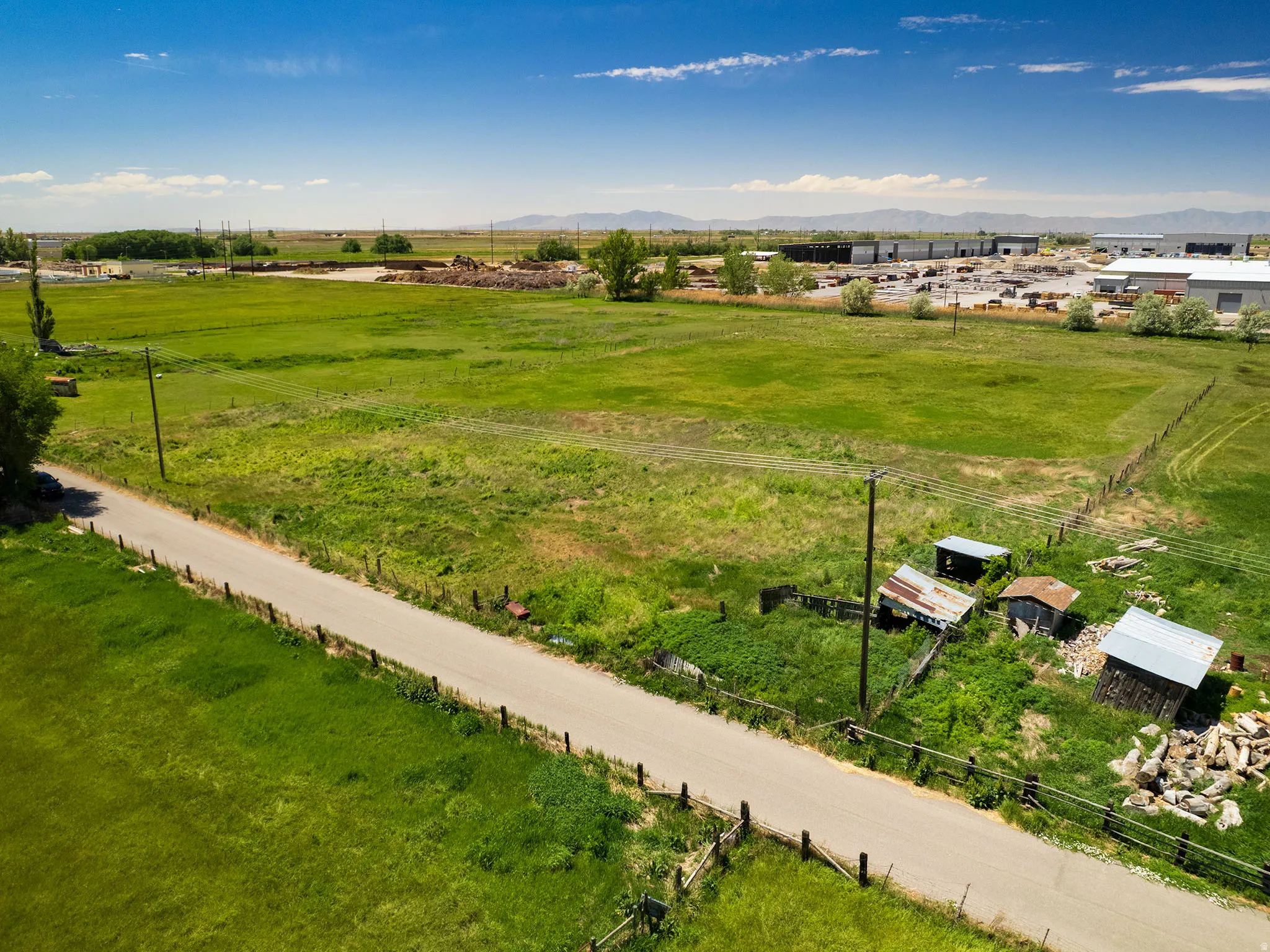 Expansive green fields with a paved road, perimeter fencing, and distant mountains