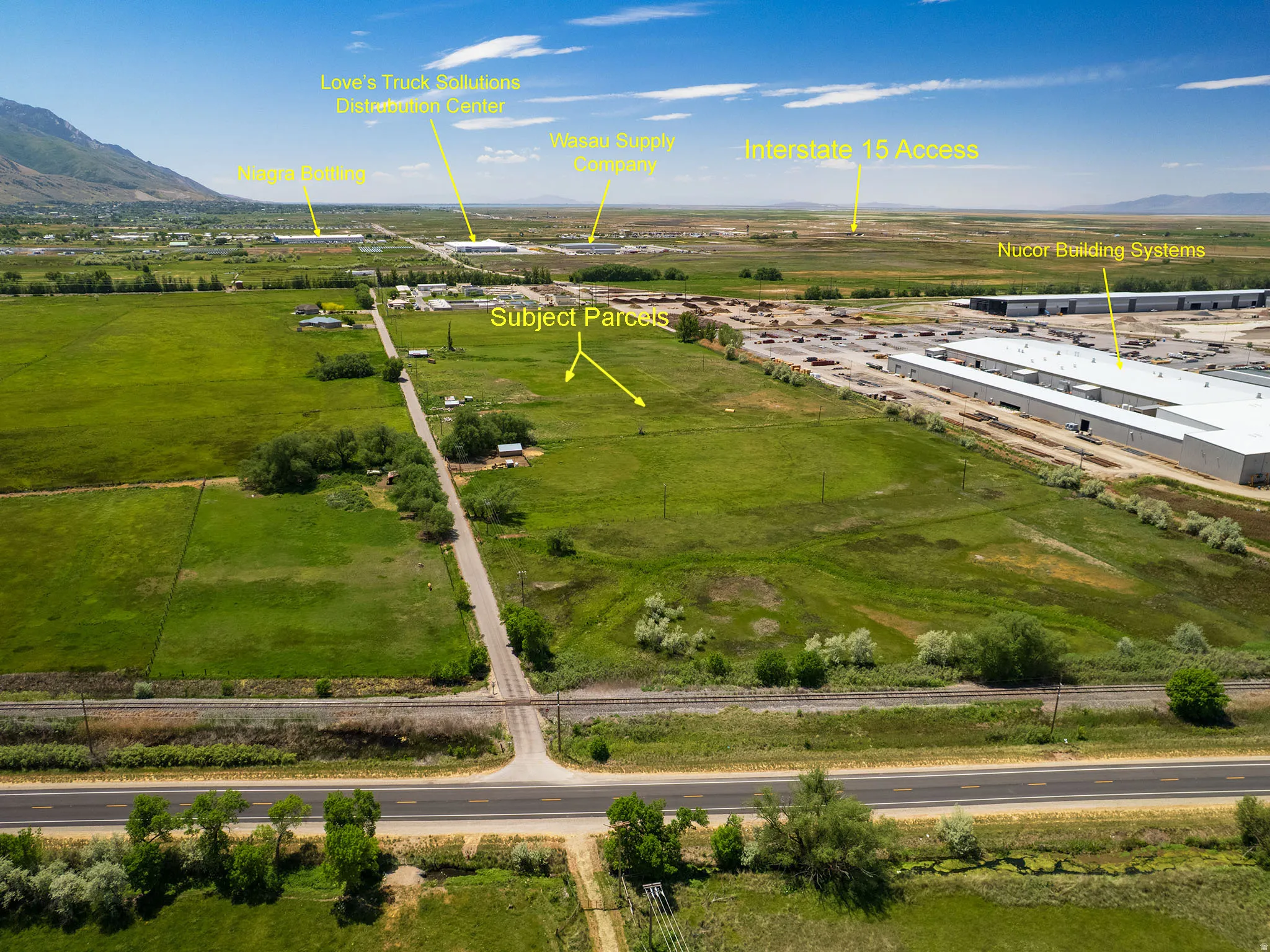 Expansive green parcels with a dirt road, bordering a highway and railroad tracks
