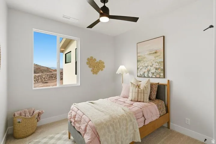 Modern bedroom featuring a large window, neutral carpeting, white baseboards, and a black ceiling fan