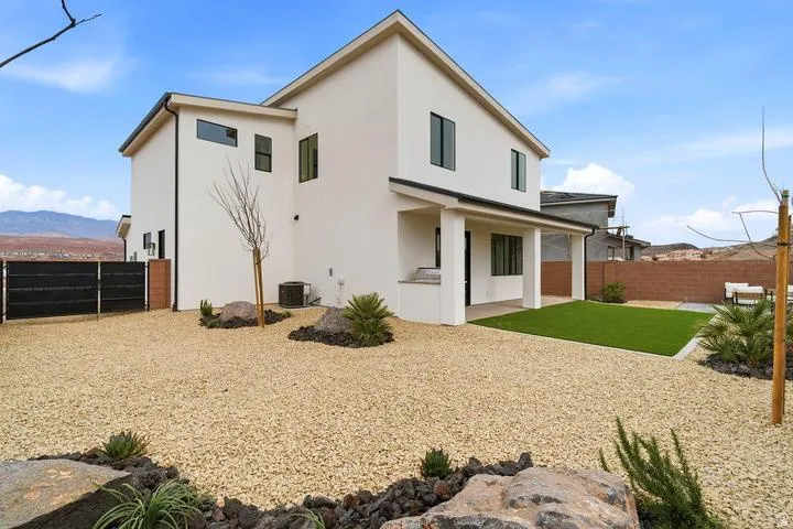 Contemporary stucco exterior with dark-framed windows, a covered patio, and a manicured artificial turf area