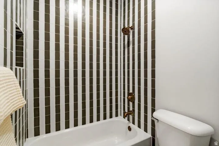 Bathtub with vertical striped black and white wall tiles, bronze-finish fixtures, and an integrated shower niche