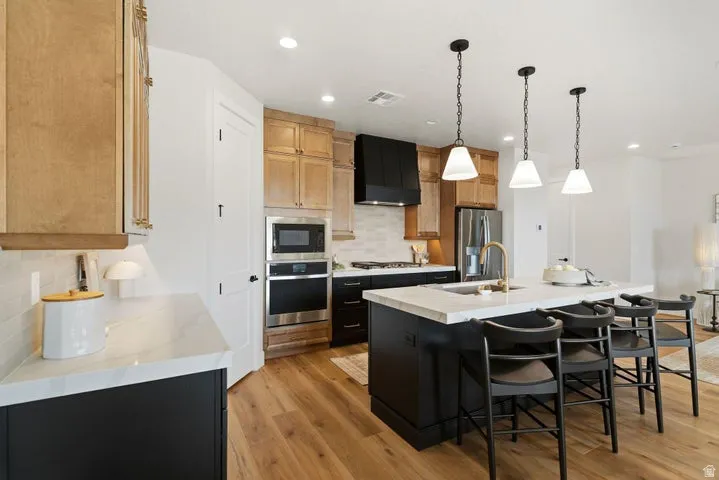 Gourmet kitchen with light wood-finish cabinetry, black island with light-toned countertop, stainless steel appliances, and wood-finish flooring