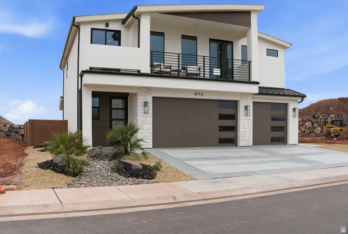 Contemporary exterior featuring a second-story balcony with black metal railings, a stone veneer facade accent, and two garage doors with frosted glass inserts