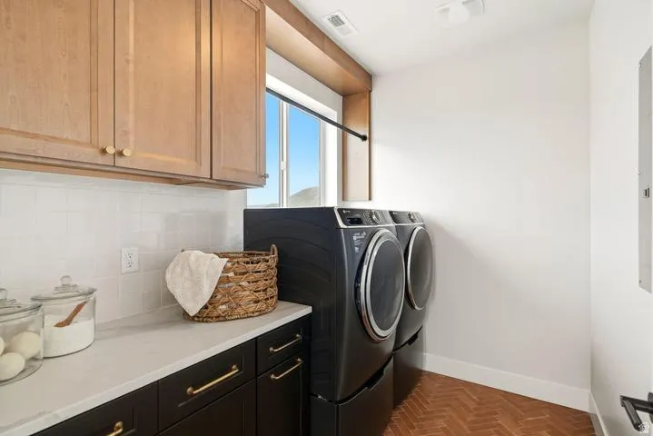 Dedicated laundry area featuring wood-finish upper cabinetry, lower cabinetry with brass hardware, and a light-toned countertop