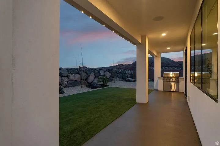 Covered patio featuring an outdoor grill station with stainless steel appliances, large format windows, recessed lighting, and a manicured lawn area