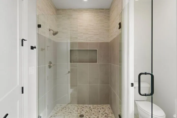 Glass-enclosed shower featuring a mosaic pebble floor, tiled shower walls, and a built-in shower niche