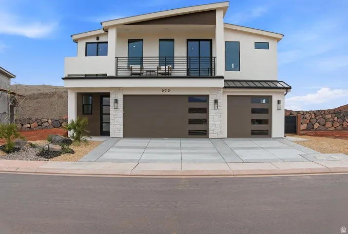 Contemporary two-story exterior featuring a balcony with black railings, two integrated garage doors with frosted glass panels, and contrasting stone accents