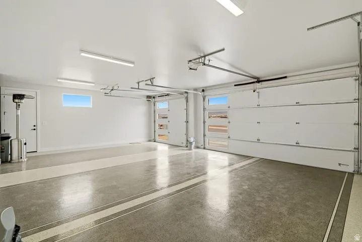 Spacious garage featuring a durable epoxy floor coating with decorative stripes, multiple overhead fluorescent light fixtures, a high ceiling, and two garage doors with upper window panels