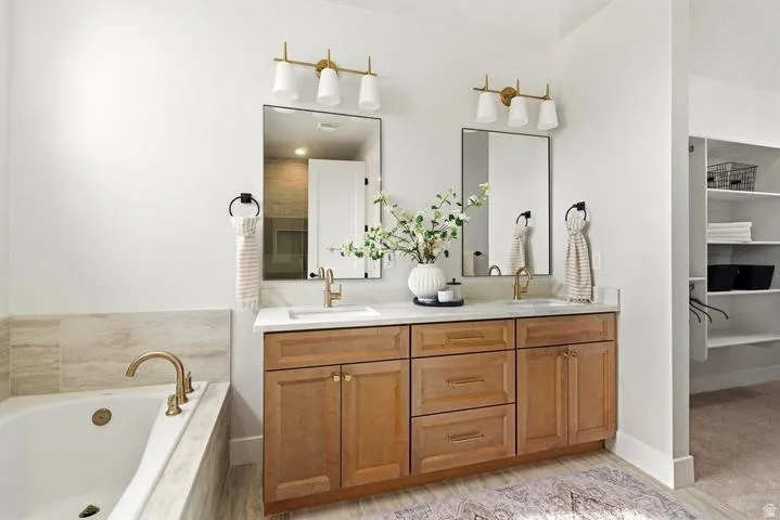 Dual vanity with brass fixtures and hardware, framed mirrors, and a built-in soaking tub with coordinating tile surround