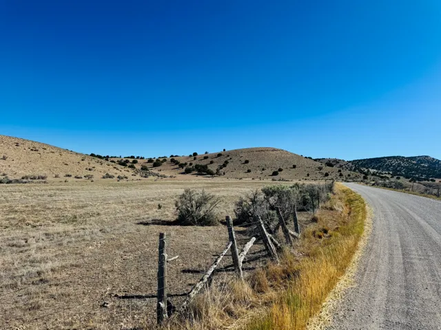 Expansive rural landscape featuring a gravel road, natural fencing, and rolling hills with scattered shrubbery