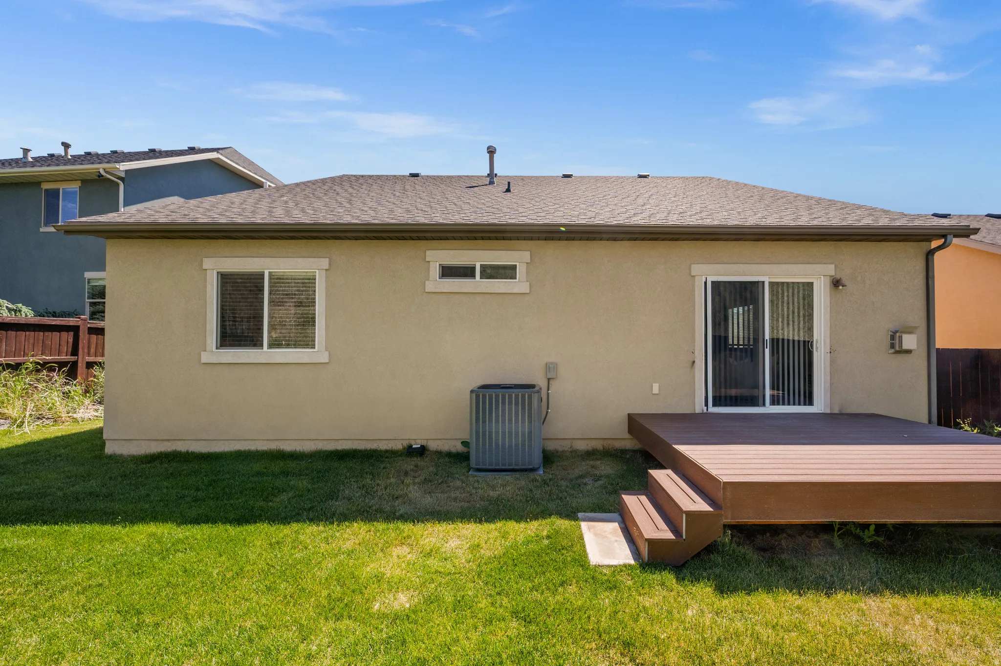 Rear exterior featuring a spacious composite deck with steps, a sliding glass door, stucco siding, and a shingle roof