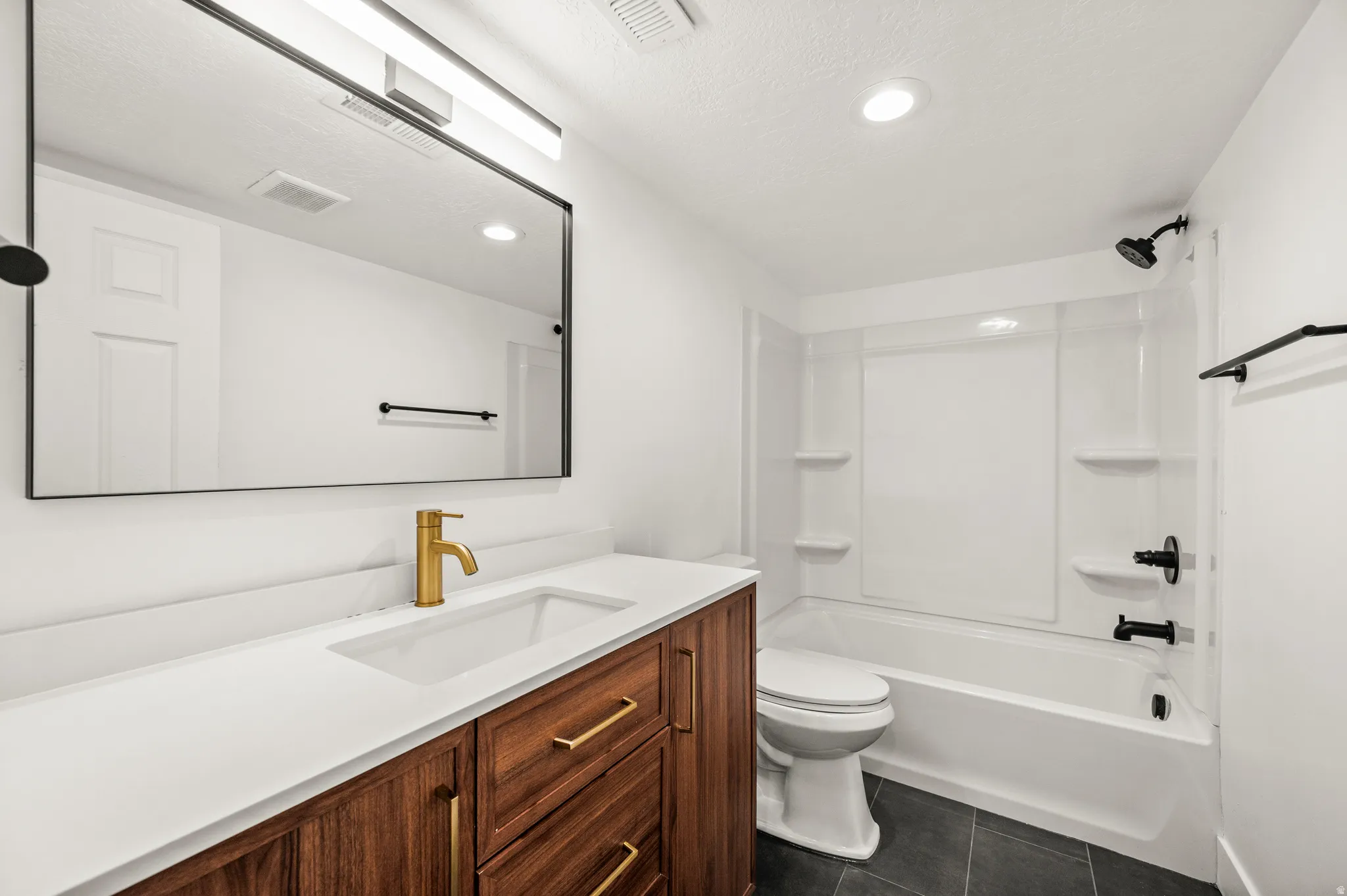 Bathroom featuring a wood-finish vanity with gold-tone hardware, a white countertop with an integrated sink, and a gold-tone faucet