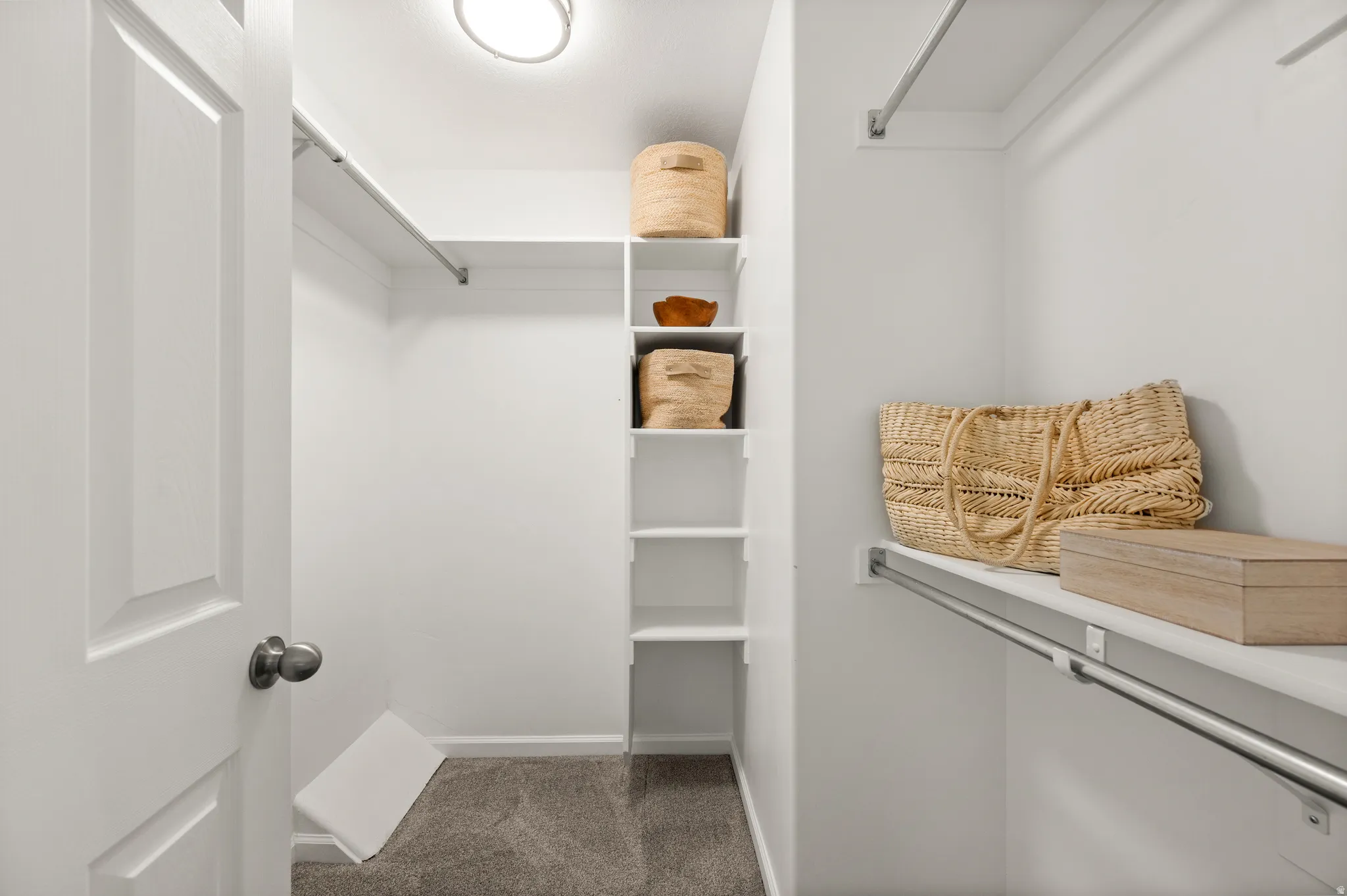 Walk-in closet featuring white paneled walls, built-in shelving, chrome hanging rods, and gray carpet flooring