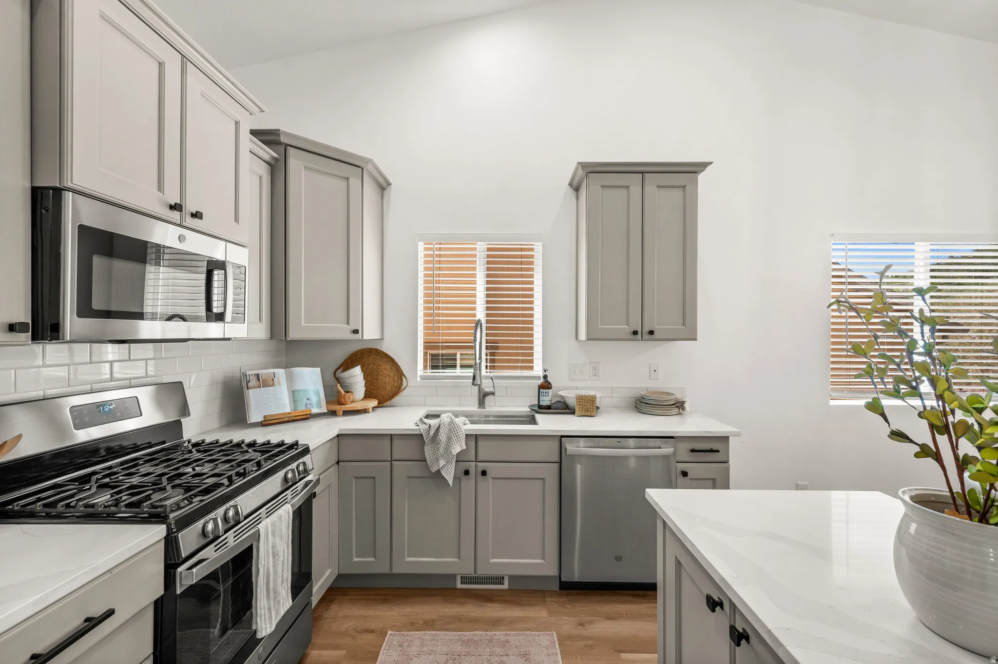 Kitchen featuring stainless steel appliances, light gray cabinetry with black hardware, white countertops, and subway tile backsplash