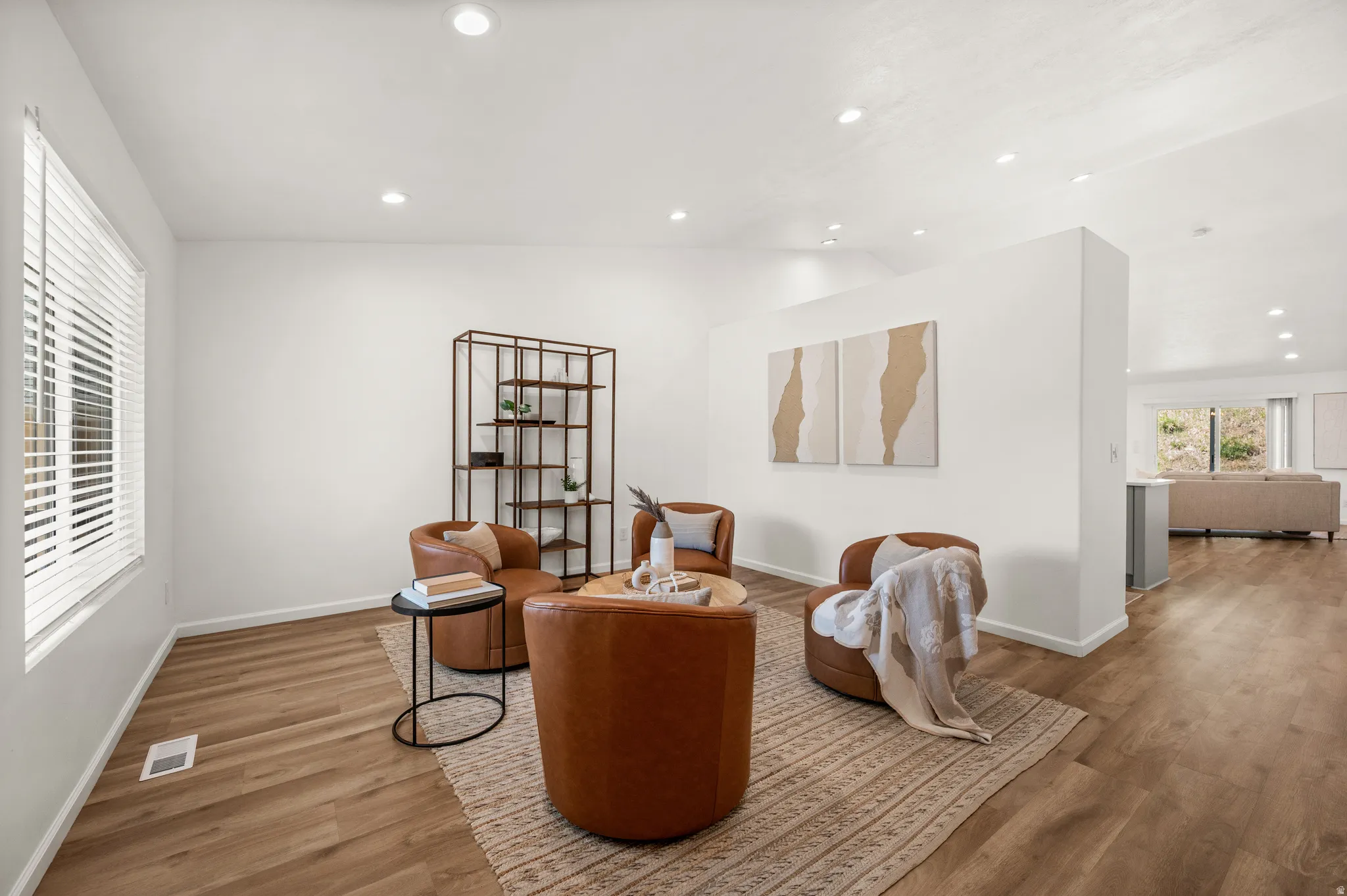 Recessed lighting illuminates this room featuring wood-finish flooring and a partial wall element
