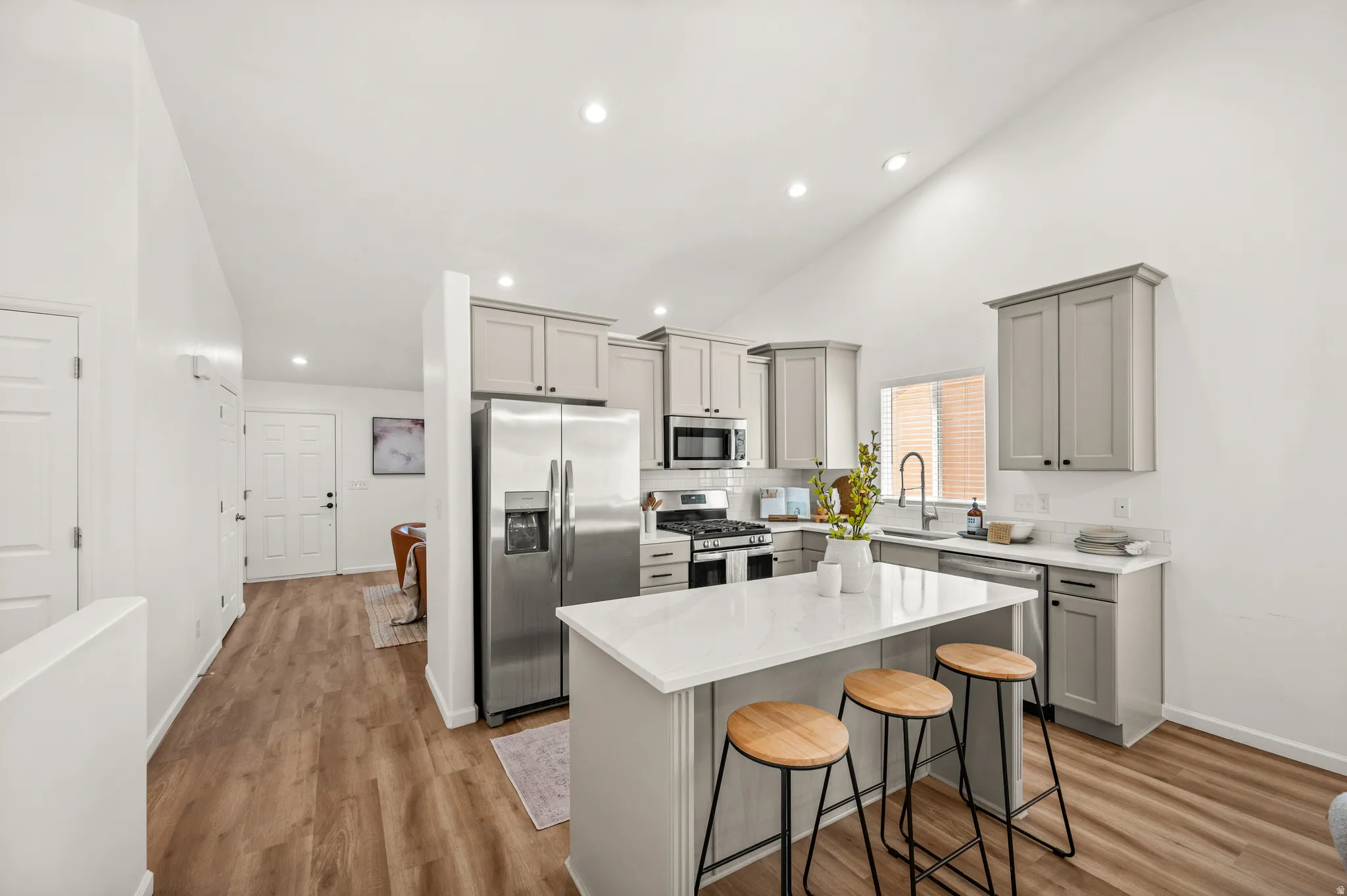 Modern kitchen featuring light gray cabinetry, stainless steel appliances, a center island with a white countertop, and wood-finish flooring