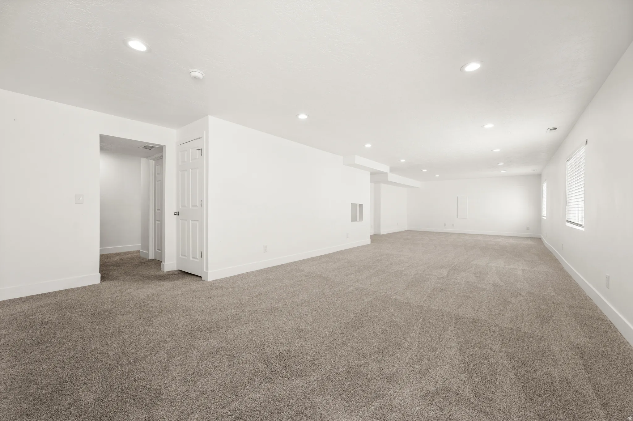 Expansive carpeted room featuring recessed lighting, white walls, multiple windows with blinds, and white trim