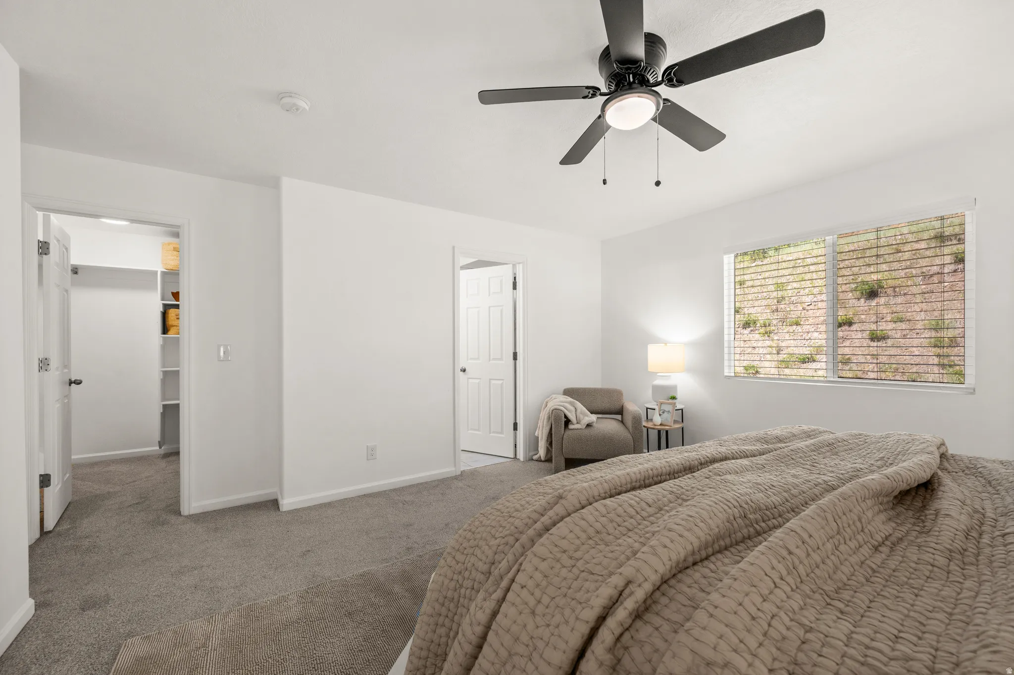 Spacious bedroom featuring neutral carpeting, a ceiling fan with integrated lighting, and a window with horizontal blinds