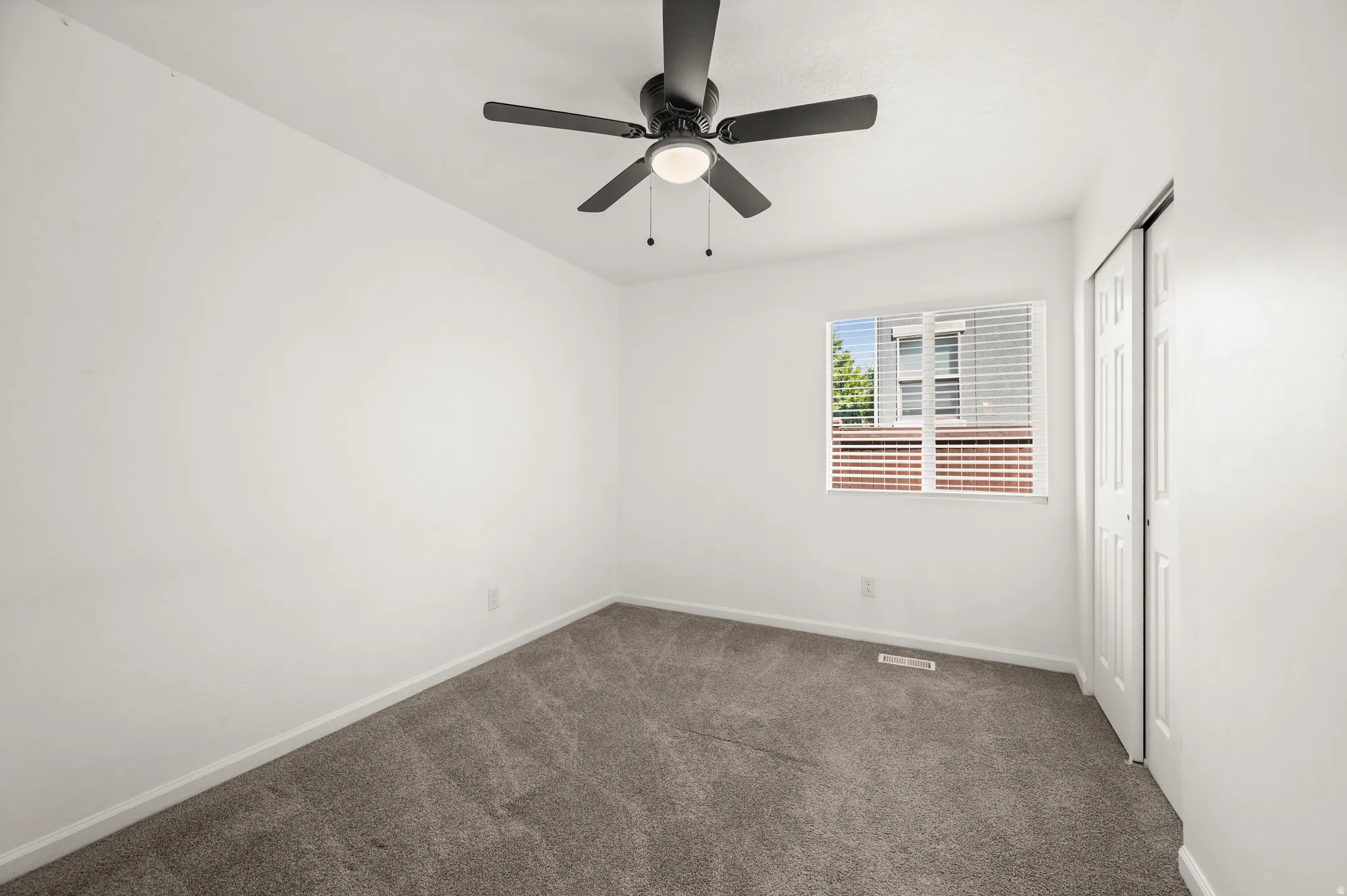 Carpeted room with white walls, a single window featuring horizontal blinds, and a bi-fold door closet