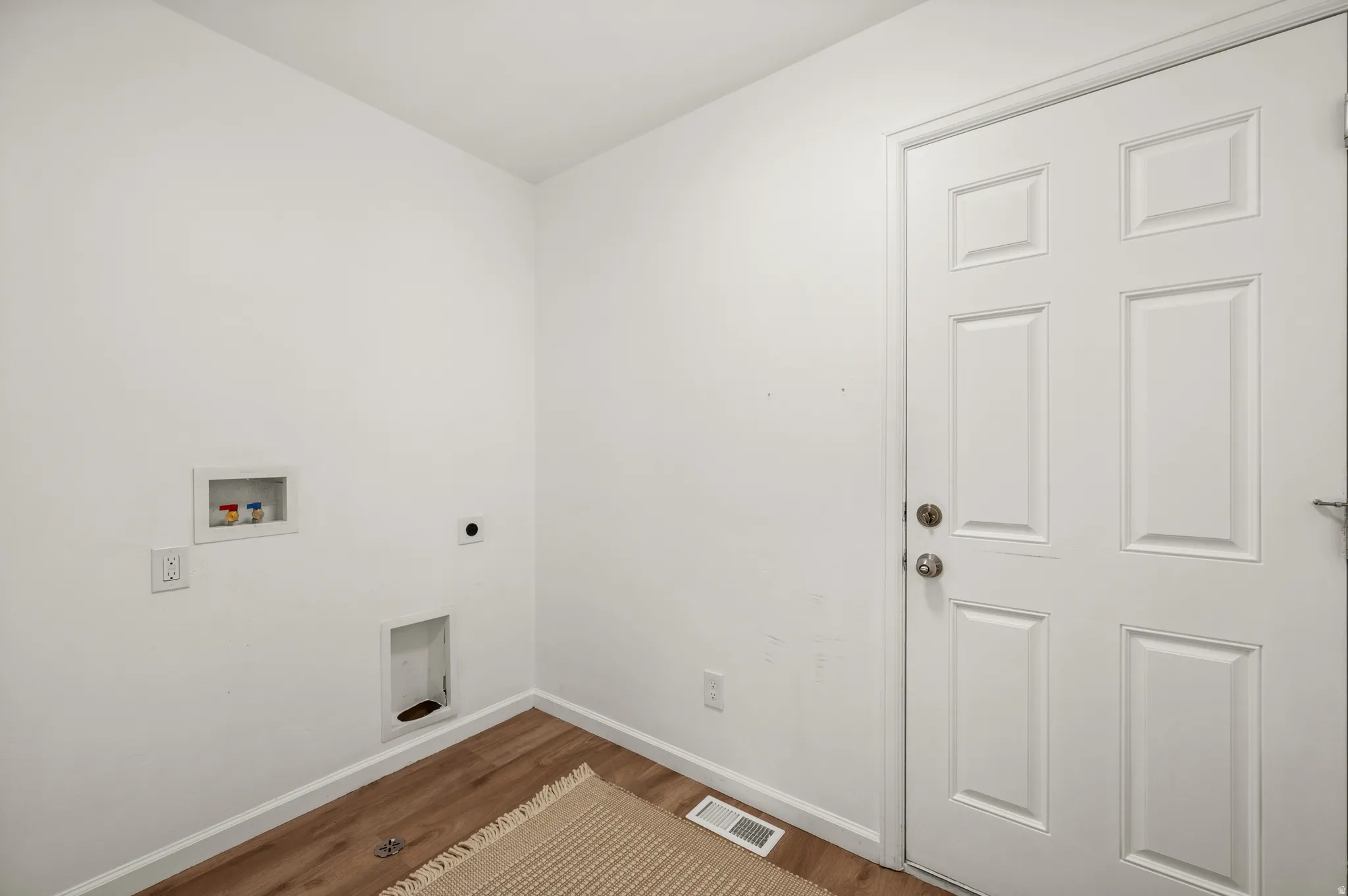 Dedicated laundry area featuring wood-finish flooring, white walls, and a multi-panel door
