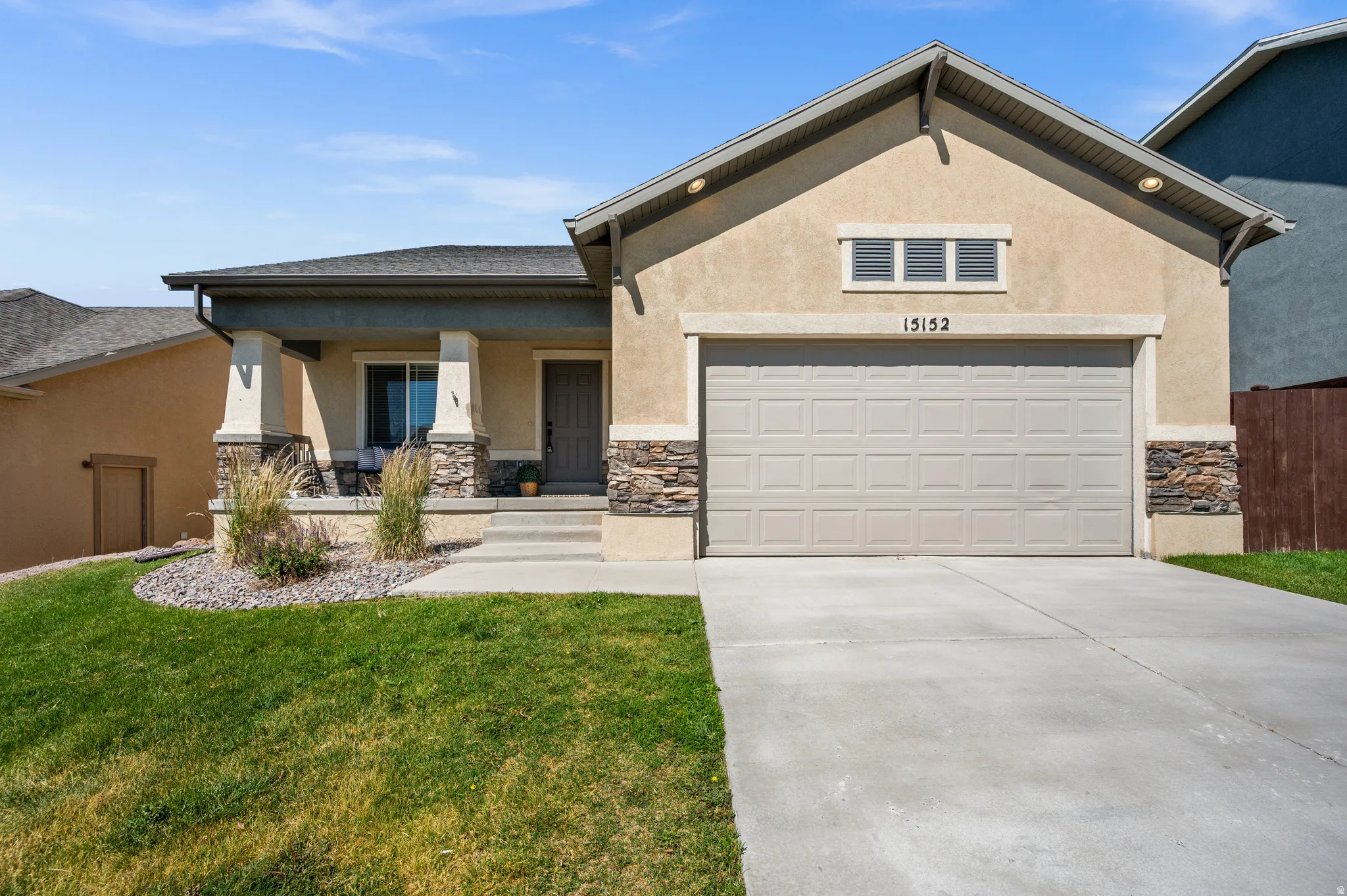 Contemporary stucco exterior featuring a covered front porch with stone accents, a two-car garage, and a concrete driveway