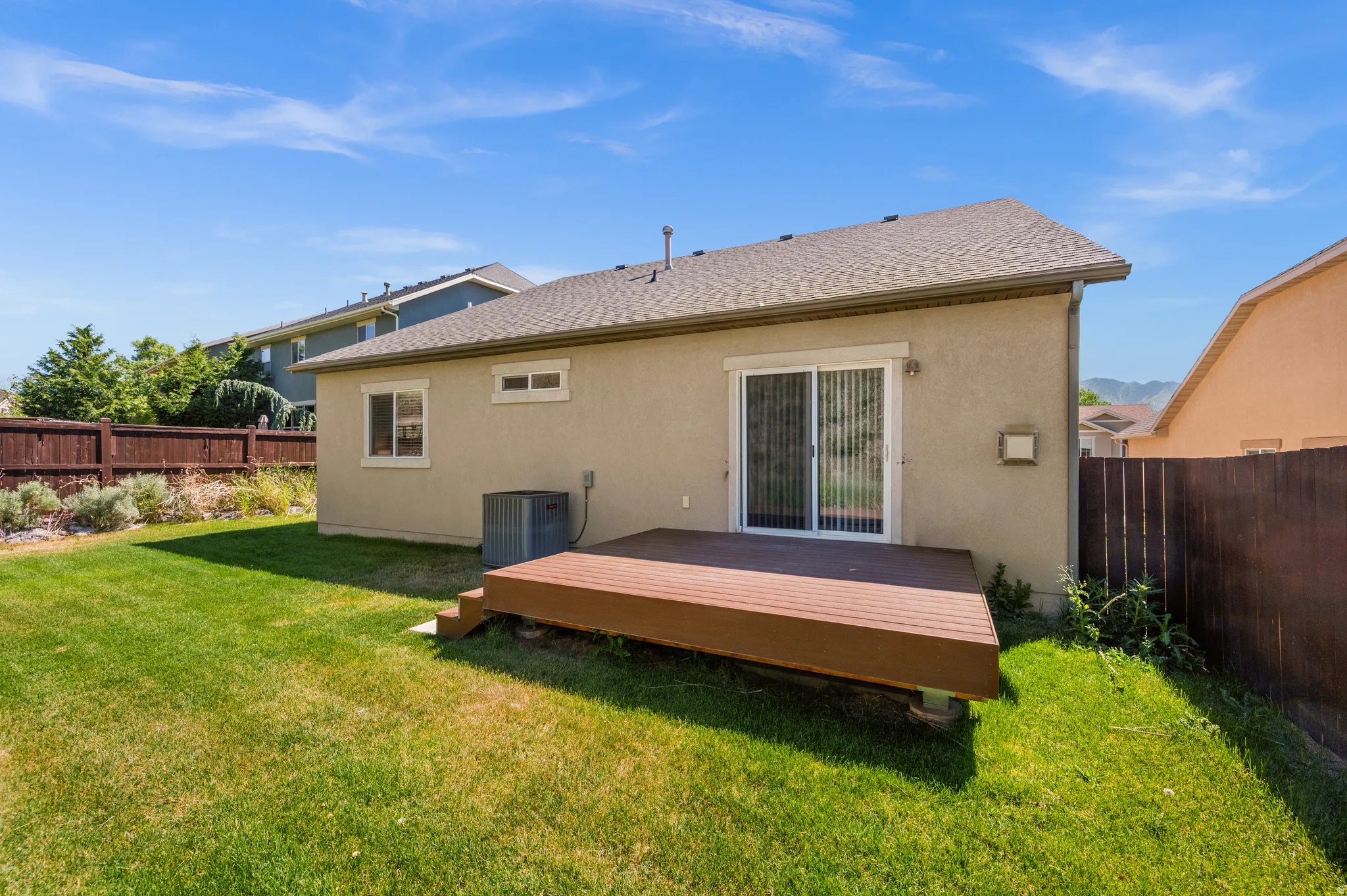 Rear exterior featuring a sliding glass door, an elevated wood-tone deck, and a fenced yard with a grass lawn