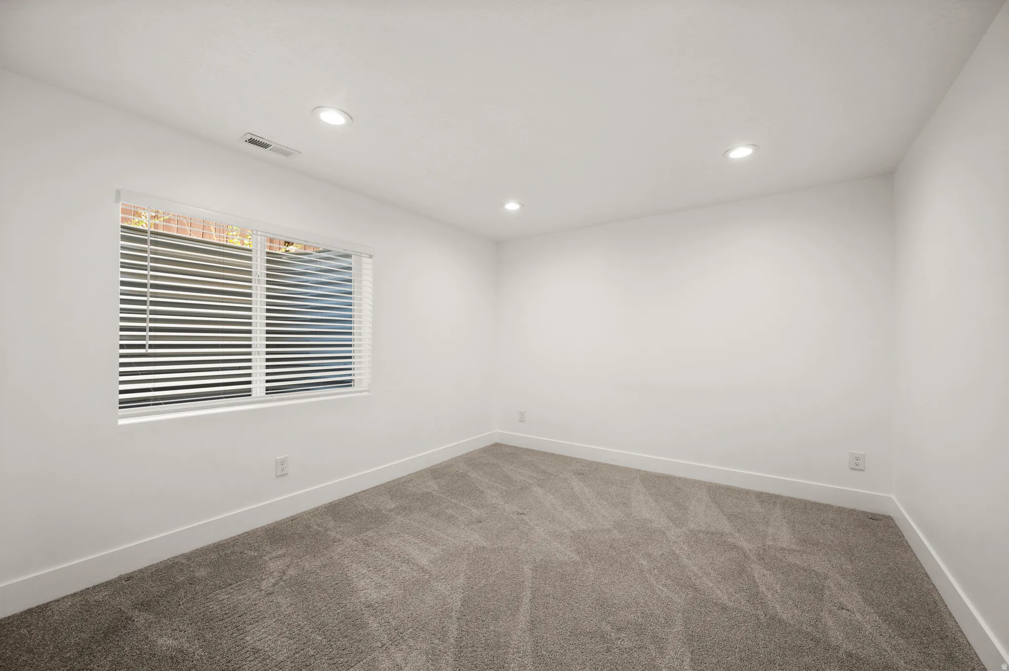 Spacious room featuring neutral carpet, white walls, recessed lighting, and a window with horizontal blinds