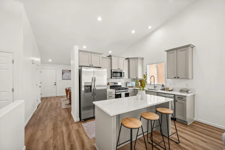 Modern kitchen featuring light gray cabinetry, stainless steel appliances, a center island with a white countertop, and wood-finish flooring