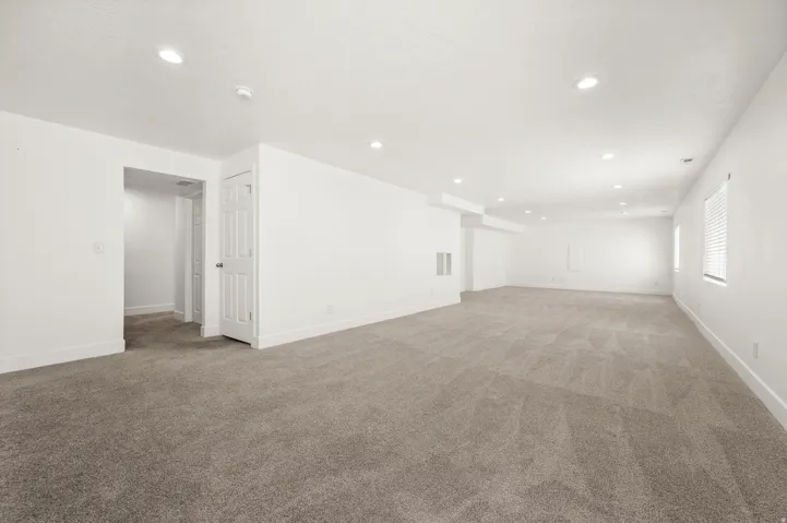 Expansive carpeted room featuring recessed lighting, white walls, multiple windows with blinds, and white trim