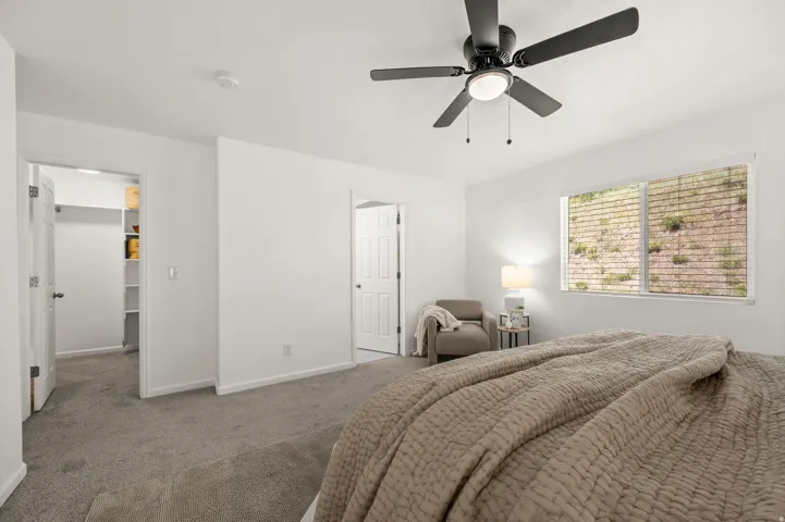 Spacious bedroom featuring neutral carpeting, a ceiling fan with integrated lighting, and a window with horizontal blinds