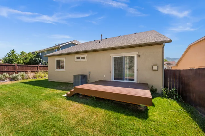 Rear exterior featuring a sliding glass door, an elevated wood-tone deck, and a fenced yard with a grass lawn