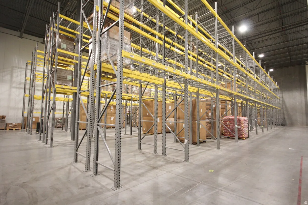 Expansive warehouse space featuring high-bay ceilings, concrete flooring, and extensive metal racking systems with yellow beams