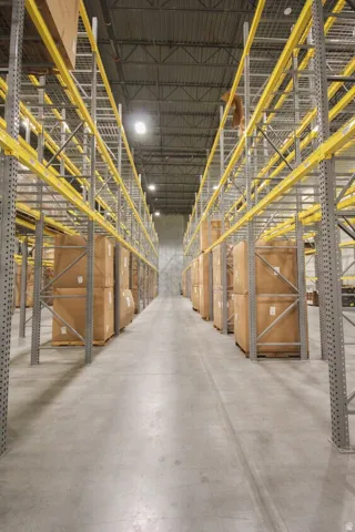 Warehouse interior featuring high ceilings, extensive metal racking systems, concrete flooring, and overhead lighting