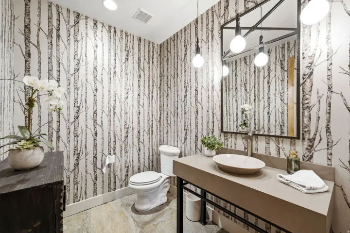 Powder room featuring tree-patterned wallpaper, a vessel sink with wall-mounted faucet, and a large framed mirror with integrated spherical lighting