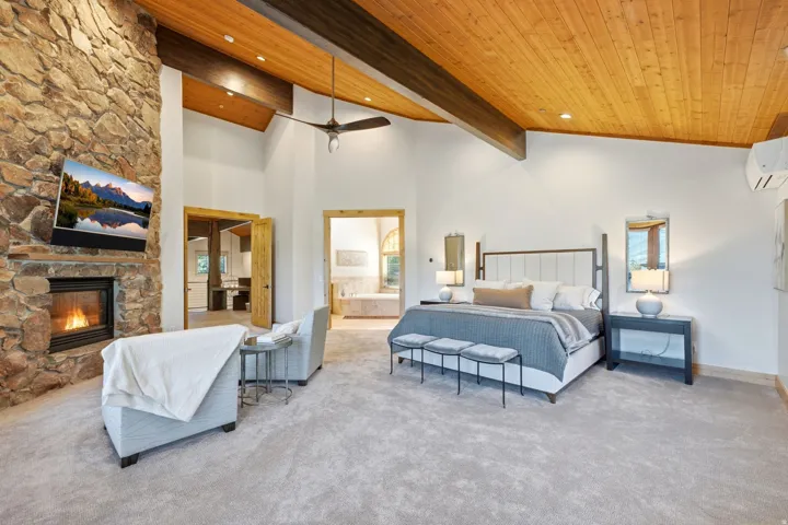 Spacious interior featuring a stone fireplace, vaulted wood-paneled ceiling, exposed wood beams, and neutral carpeting