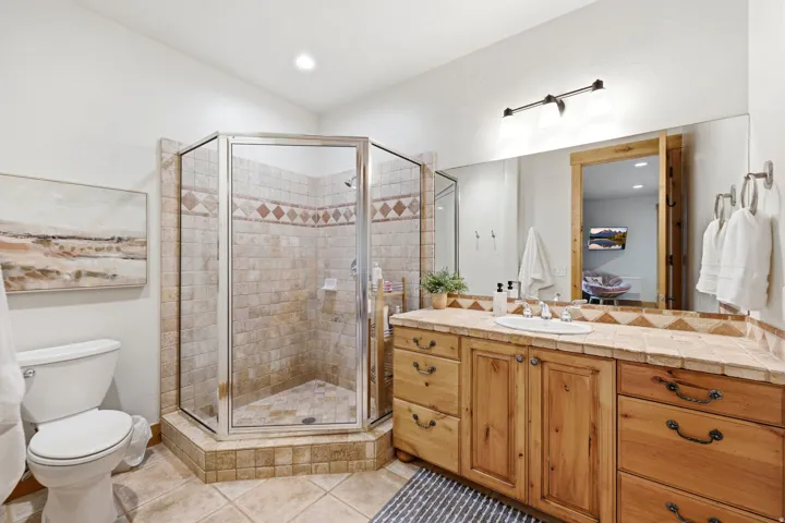 Tile-surround shower with glass enclosure, single vanity with wood cabinetry, and a tile countertop
