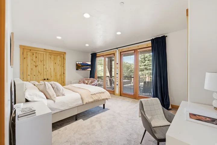 Bright bedroom featuring double French doors leading to an outdoor balcony, recessed lighting, light wood-finish bi-fold closet doors, and carpeted flooring