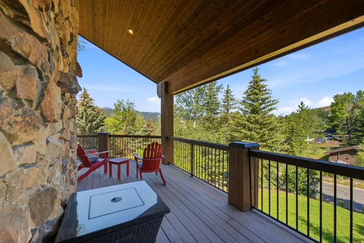 Expansive outdoor deck featuring a stone-clad exterior wall, wood-finish ceiling, durable composite decking, and metal railing