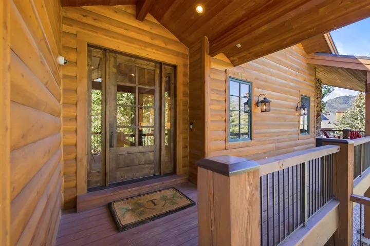 Wood-sided exterior featuring a glass-paned entry door with sidelights, a covered porch with wood railings and black vertical balusters, and wall-mounted exterior light fixtures