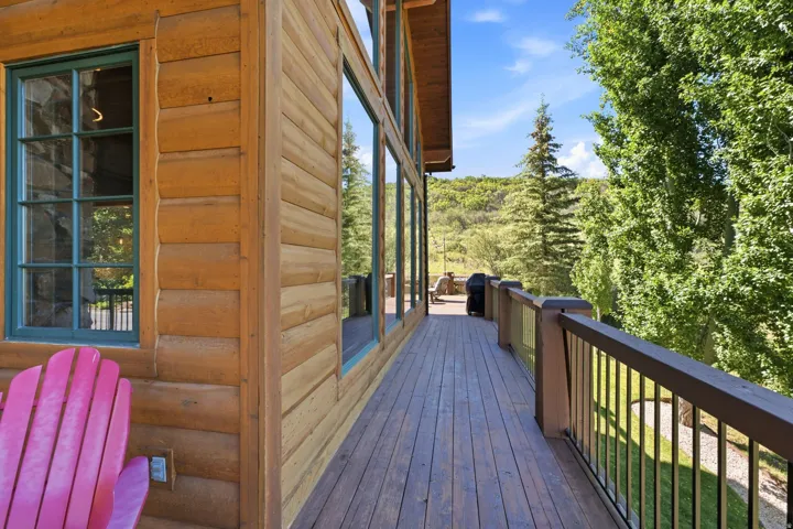 Expansive exterior deck featuring wood-finish flooring, a metal railing system, and a natural wood-sided structure with large windows