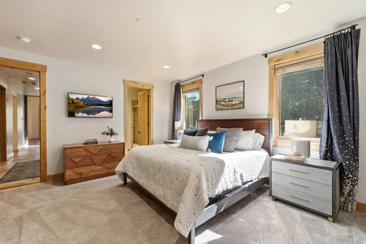 Light-toned carpeting enhances this sleeping area featuring two windows with natural wood trim