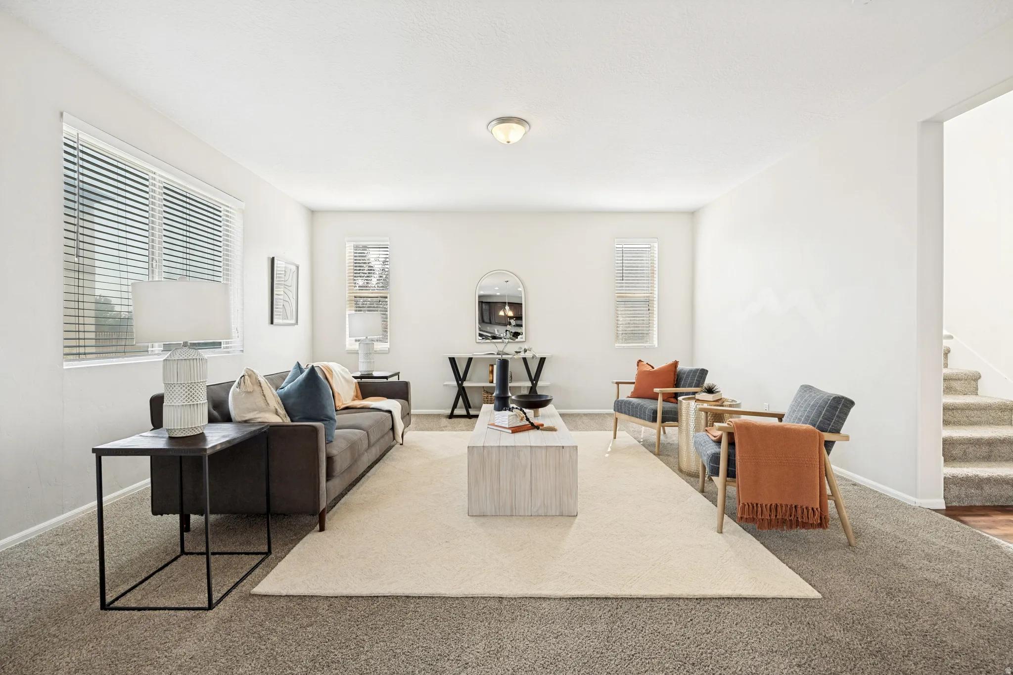 Light-filled living area featuring neutral carpeting, white walls, and multiple windows with blinds