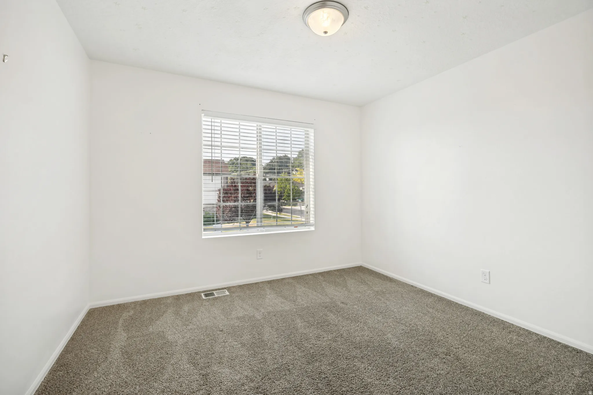 Room featuring neutral-toned walls, gray patterned carpeting, and a window with horizontal blinds