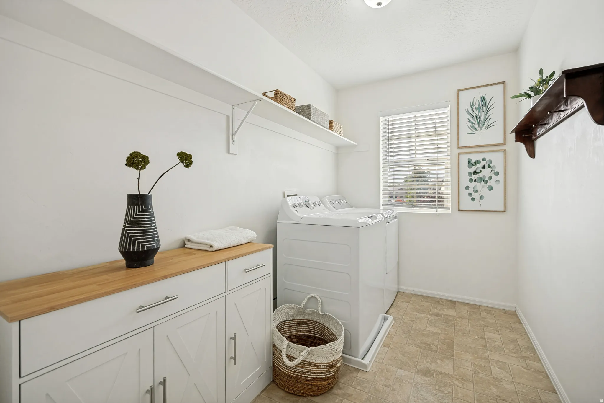 Dedicated laundry room featuring light-toned flooring, a window with blinds, and white built-in cabinetry with a wood-finish countertop