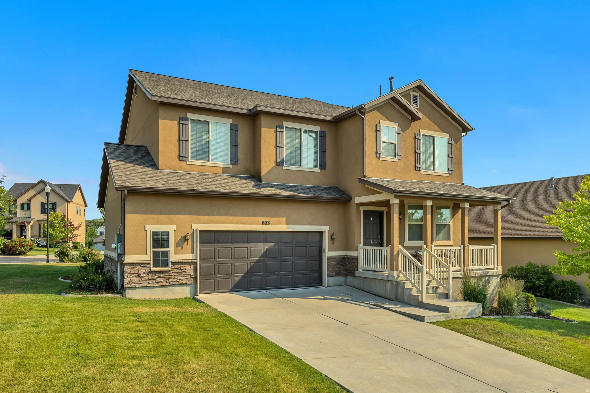 Two-story residence featuring a stucco exterior, stone facade accents, and a covered front porch with white railings