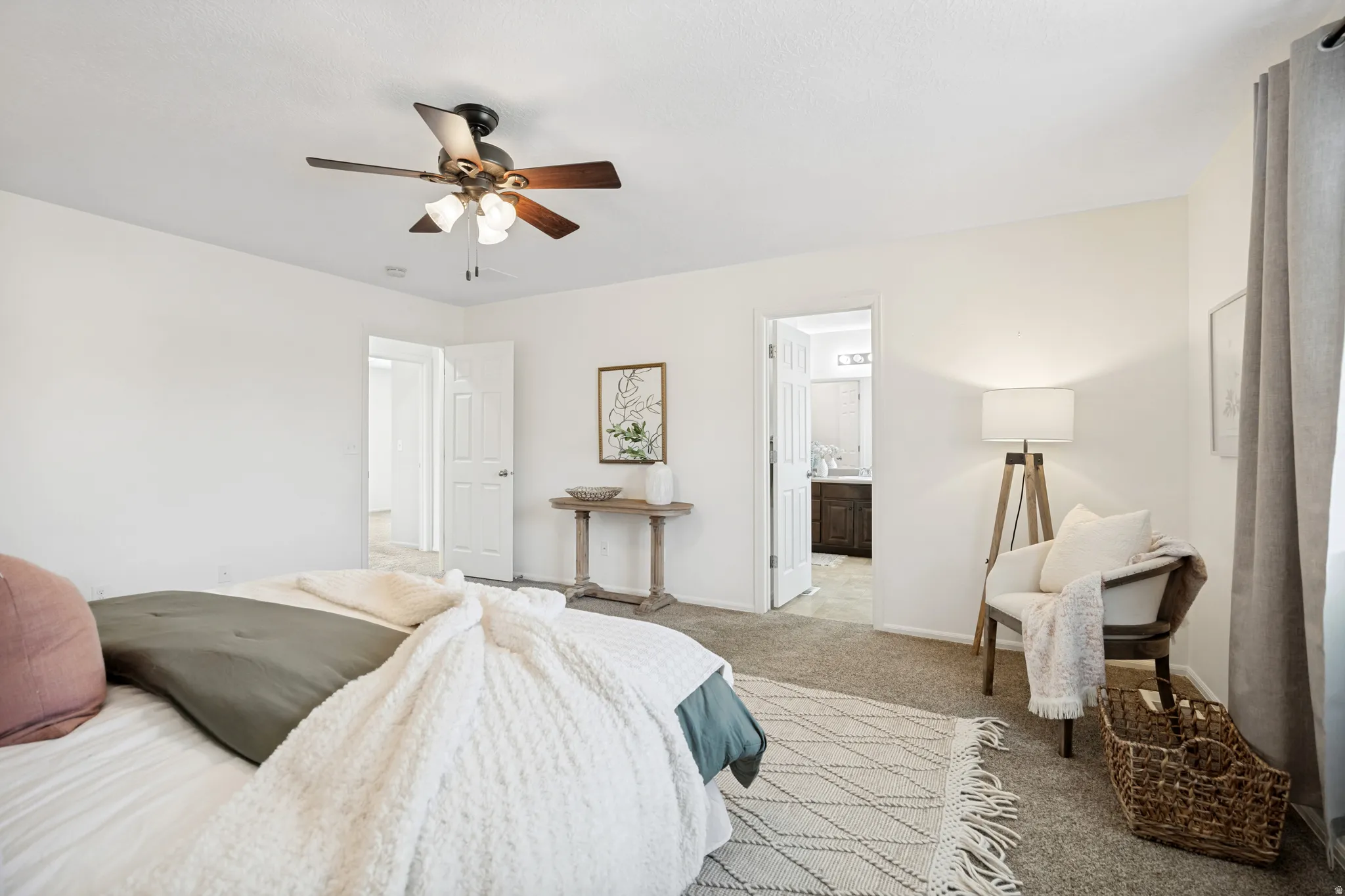 Carpeted room with a ceiling fan, white walls, and a doorway revealing a bathroom with a dark wood-finish vanity