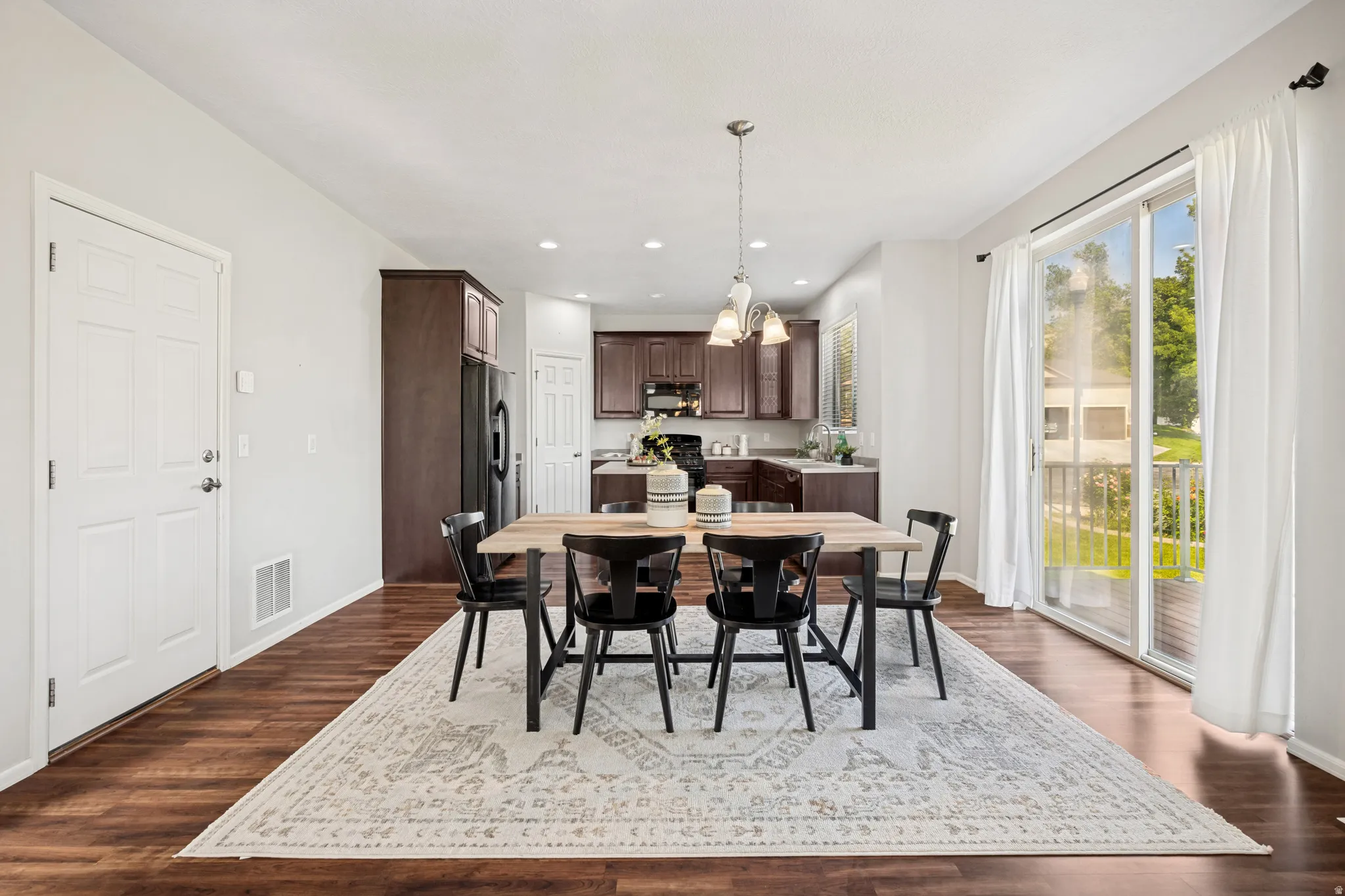 Open-concept dining area featuring wood-finish flooring, a contemporary chandelier, and a sliding glass door leading to an outdoor space