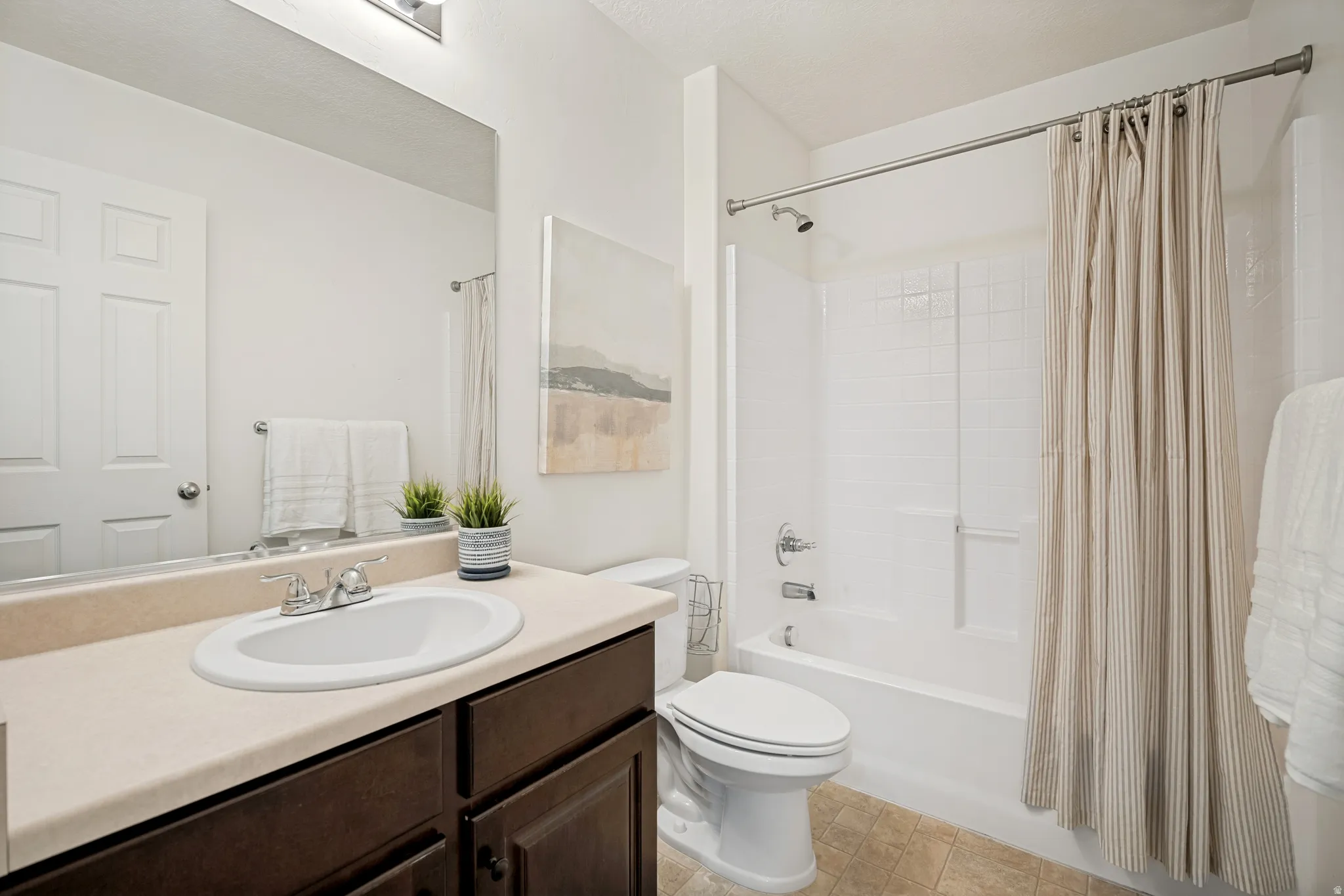Bathroom featuring a vanity with an integrated sink, a large mirror, a toilet, and a shower-over-tub combination with white subway tile surround