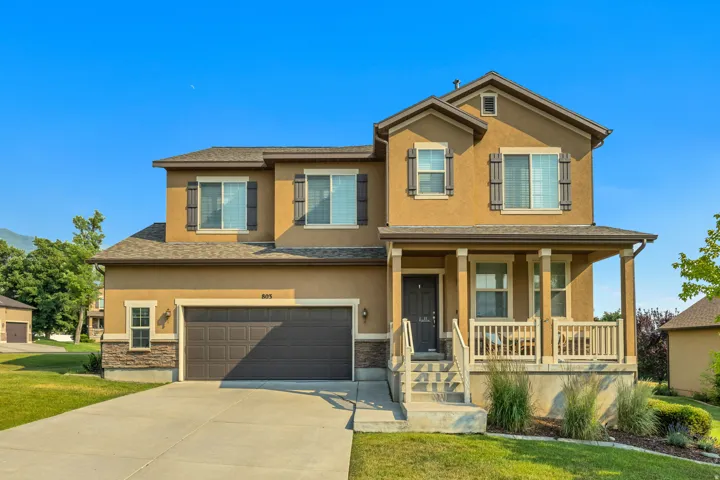Two-story stucco residence featuring a covered front porch with white railings, an attached two-car garage, and a concrete driveway