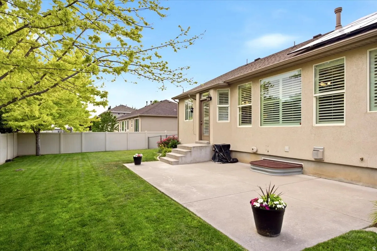 Expansive backyard featuring a manicured lawn, full vinyl privacy fencing, mature trees, and a concrete patio